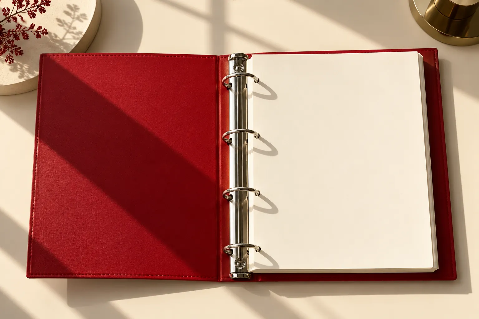 Open red ring binder with blank cream pages on a sunlit desk