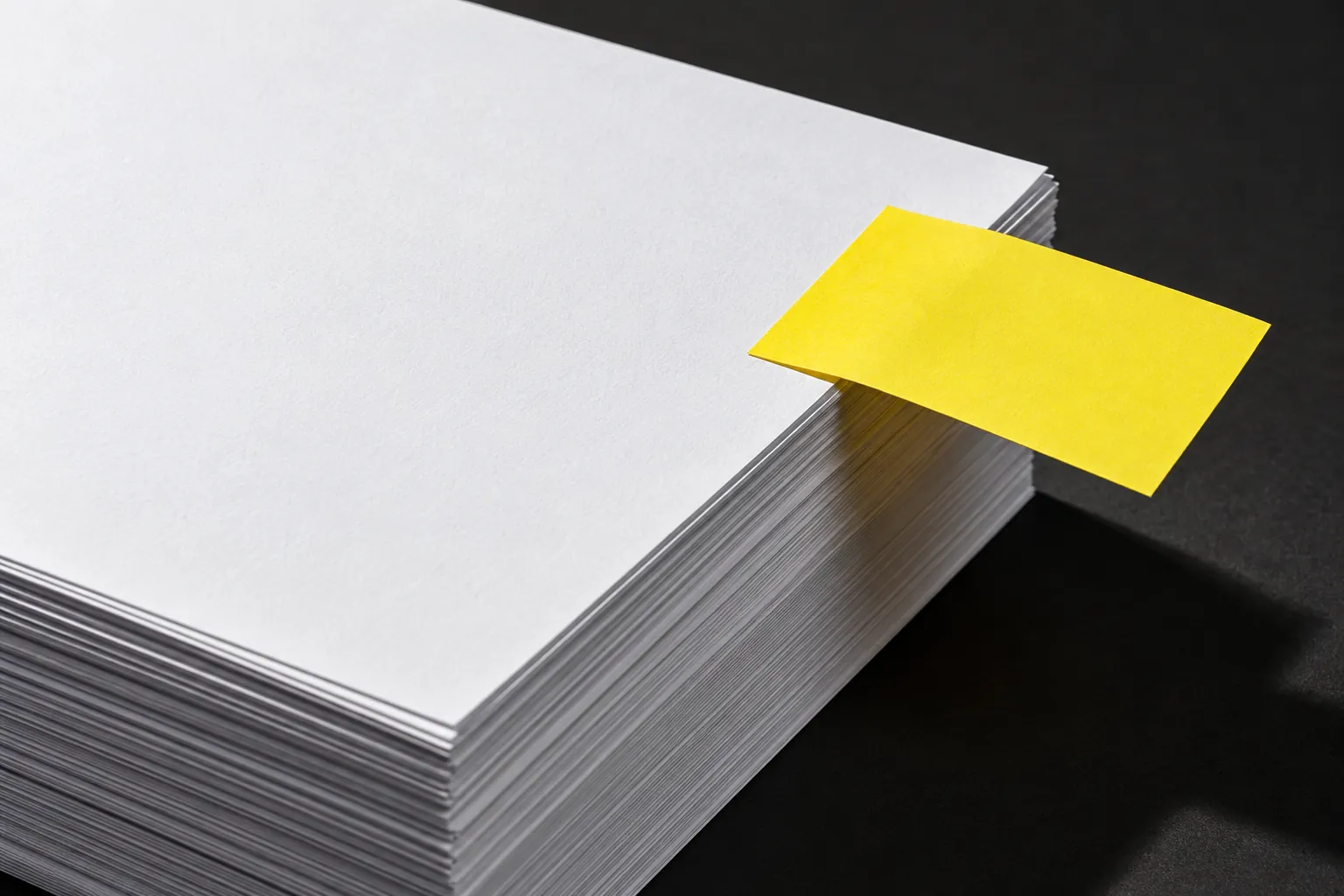 Yellow sticky note attached to a stack of blank white paper